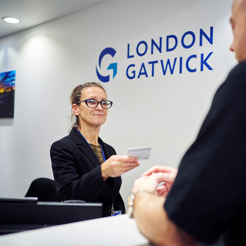 a photo of a woman checking someone's ID card, with the London Gatwick logo on the wall behind her